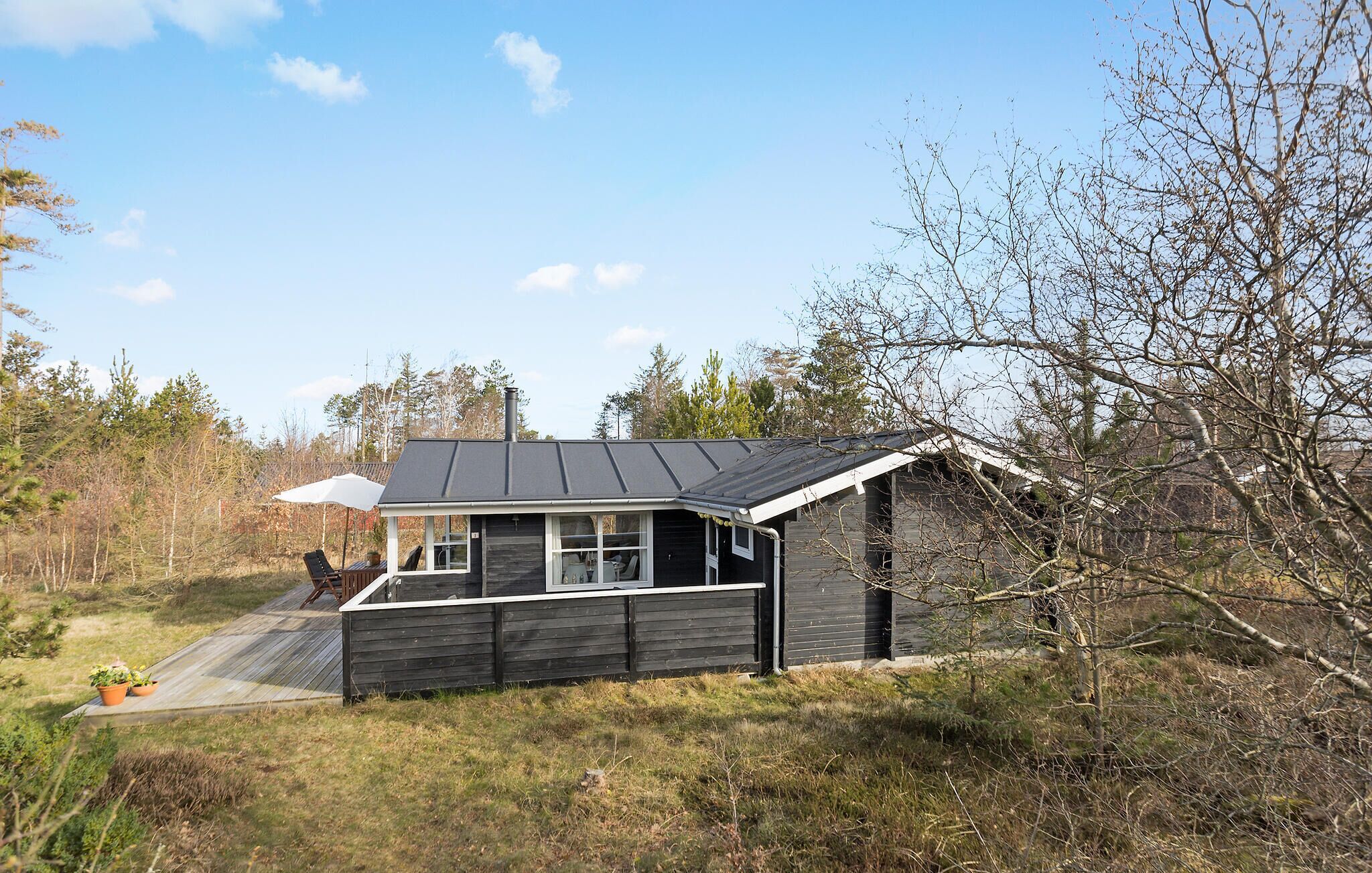 A small cabin with a dark exterior, a sloped roof, and a porch with a white umbrella.