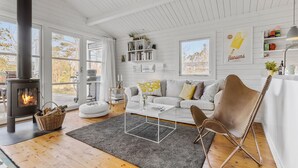Ett mysigt vardagsrum med en öppen spis, en vit soffa, ett soffbord och en fåtölj.