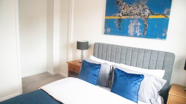 A bedroom with a bed, pillows, a nightstand, a lamp, and a painting on the wall. - Lovely 1 bed Apt - Buckinghamshire (High Wycombe)