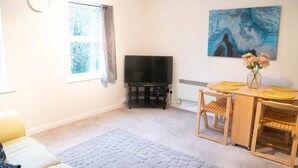 A living room with a flat-screen TV, a painting, a dining table with chairs, and a rug. - Lovely 1 bed Apt - Buckinghamshire (High Wycombe)