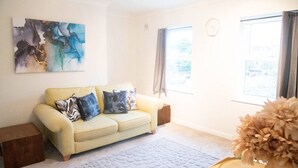 A living room with a beige sofa, a coffee table, a rug, and a painting on the wall. - Lovely 1 bed Apt - Buckinghamshire (High Wycombe)