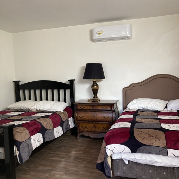 A bedroom with two single beds, a nightstand with a lamp, and an air conditioning unit on the wall.