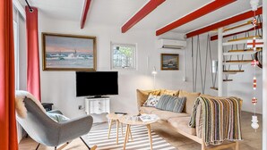 Una sala de estar con sofá, sillón, televisor y cuadros.