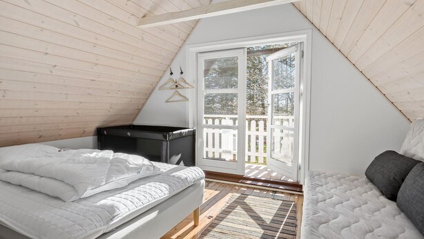 Un dormitorio con cama elevada, un escritorio pequeño y una puerta corrediza de vidrio que da a un balcón.