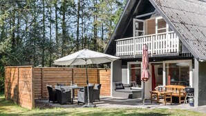 Una terraza de madera con mobiliario exterior, una mesa cubierta y una parrilla.