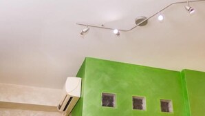 Una habitación con una pared verde, un equipo de aire acondicionado blanco y una lámpara en el techo.