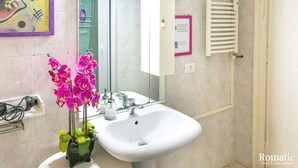 Un baño con un lavamanos blanco, un espejo, un perchero para toallas y una orquídea en maceta.
