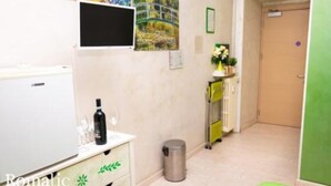 Una habitación de hotel con una cama, un pequeño escritorio con una botella y vasos, un cesto de basura y una puerta verde.