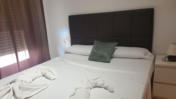 A neatly made bed with white linens and two towels folded at the foot. - Oceanografico Apartments (Valencia)