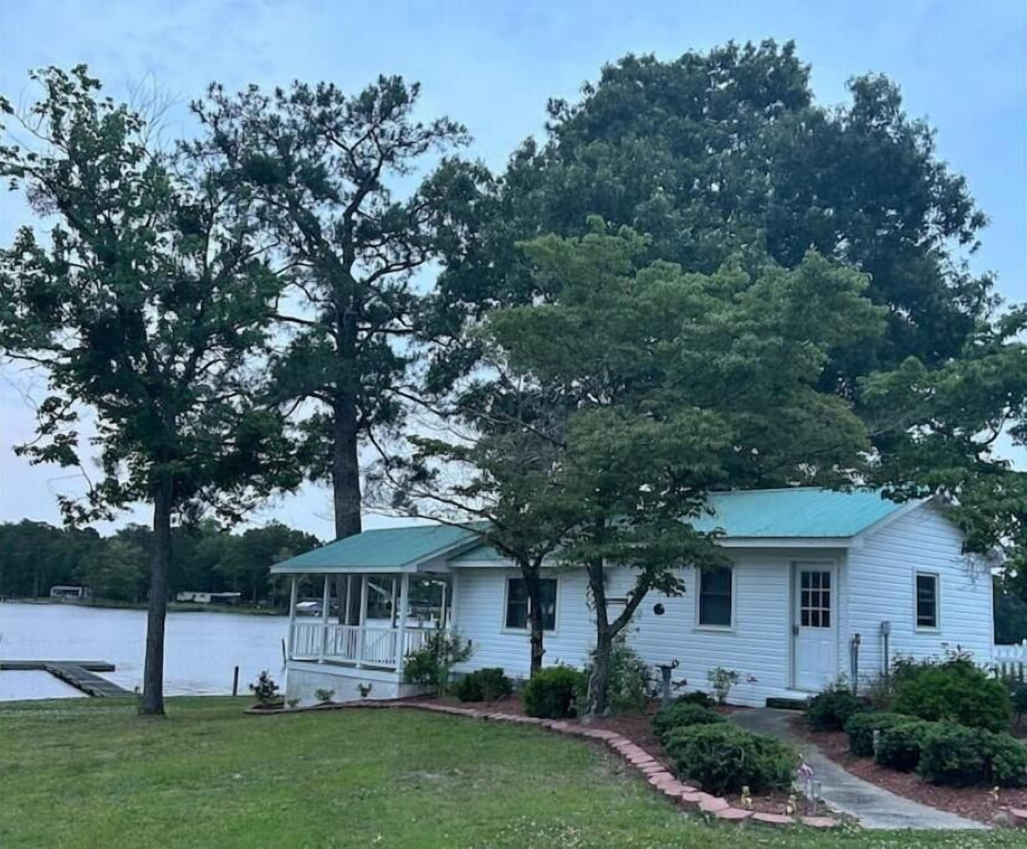 A white house with a green roof, a porch, and a small garden.