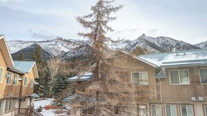 A multi-story building with a wooden facade and a balcony, set against a backdrop of snow-covered mountains. - Luxurious Retreat/Hot Tub/Mountain View/4 Beds (Bighorn No. 8)