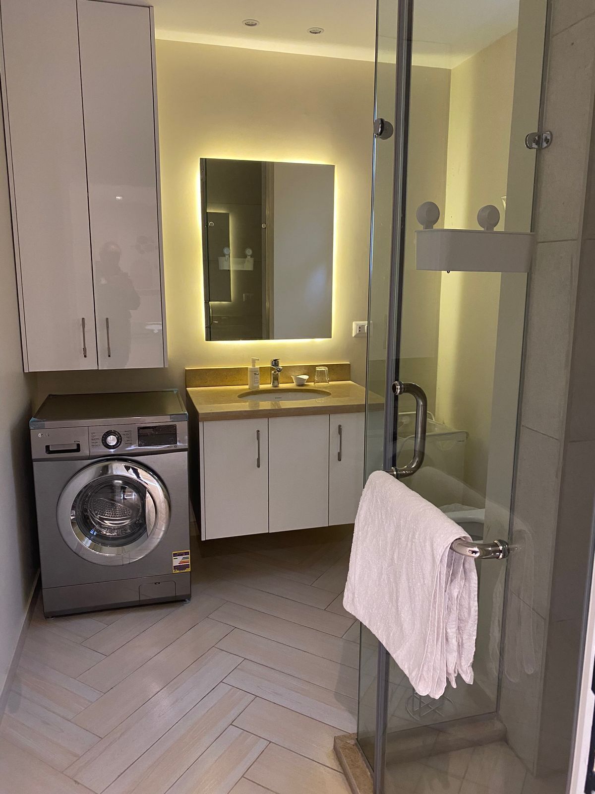 Ein modernes Badezimmer mit Waschmaschine, Duschkabine aus Glas und großem Spiegel.