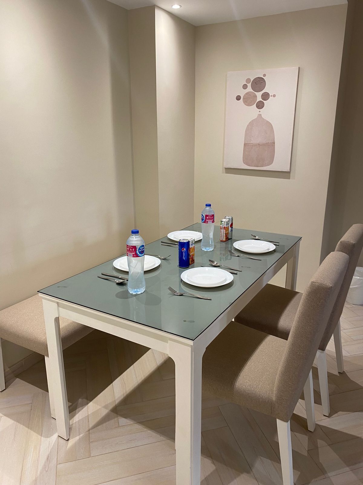 Een eetgedeelte met een glazen tafel, witte stoelen en een schilderij aan de muur.