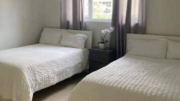 A bedroom with two single beds, a nightstand, a window with curtains, and a small potted plant.