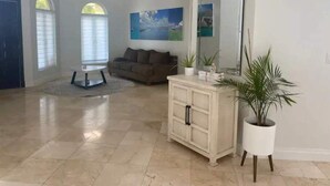 A spacious living room with a large mirror, a sofa, and a coffee table. There are potted plants and a painting on the wall. - House by the lake: 3BR/2.5BA, Gated with a Pool! (Nassau)