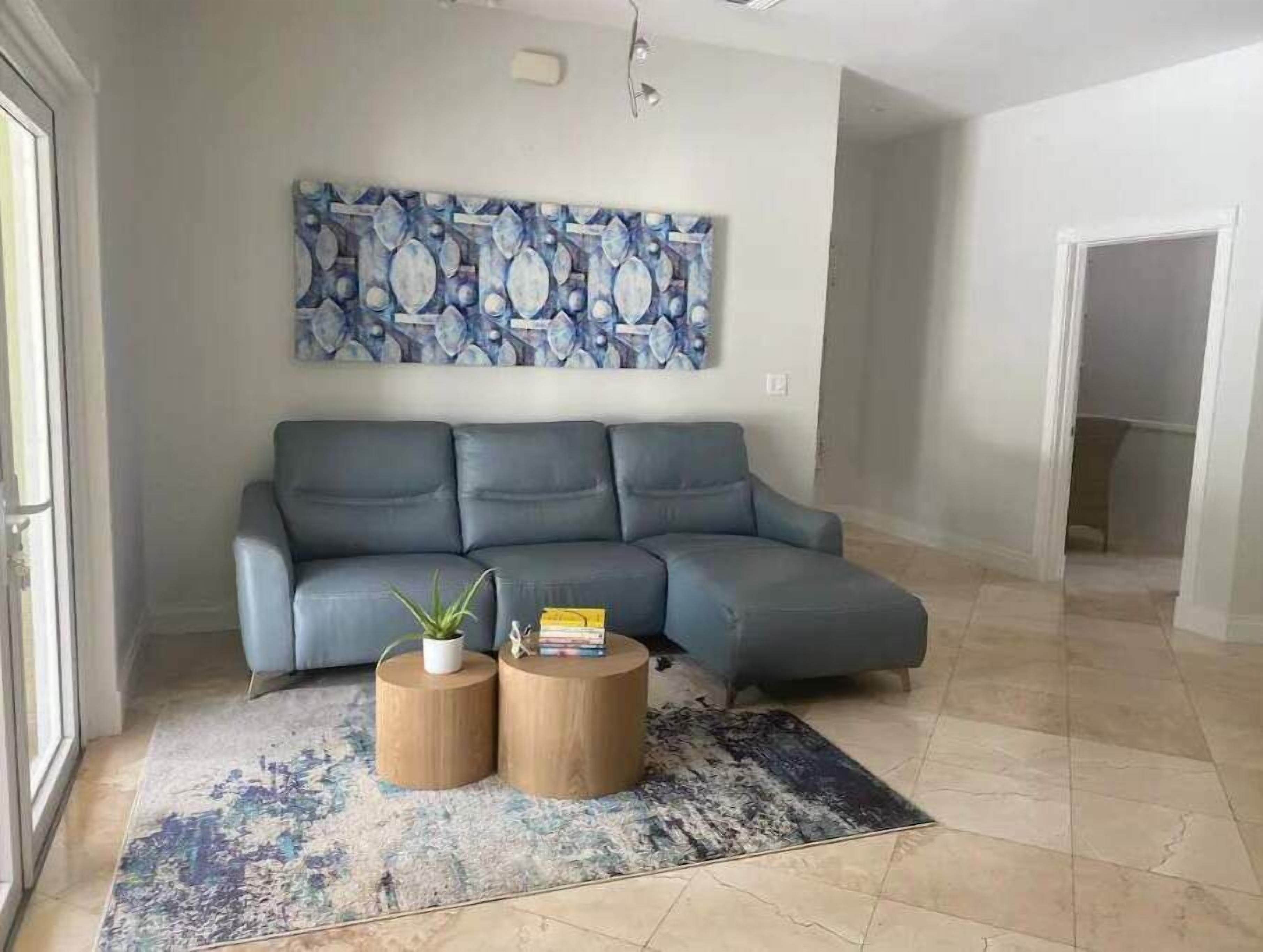 A living room with a grey sofa, two round wooden side tables, a patterned rug, and a large abstract painting on the wall.