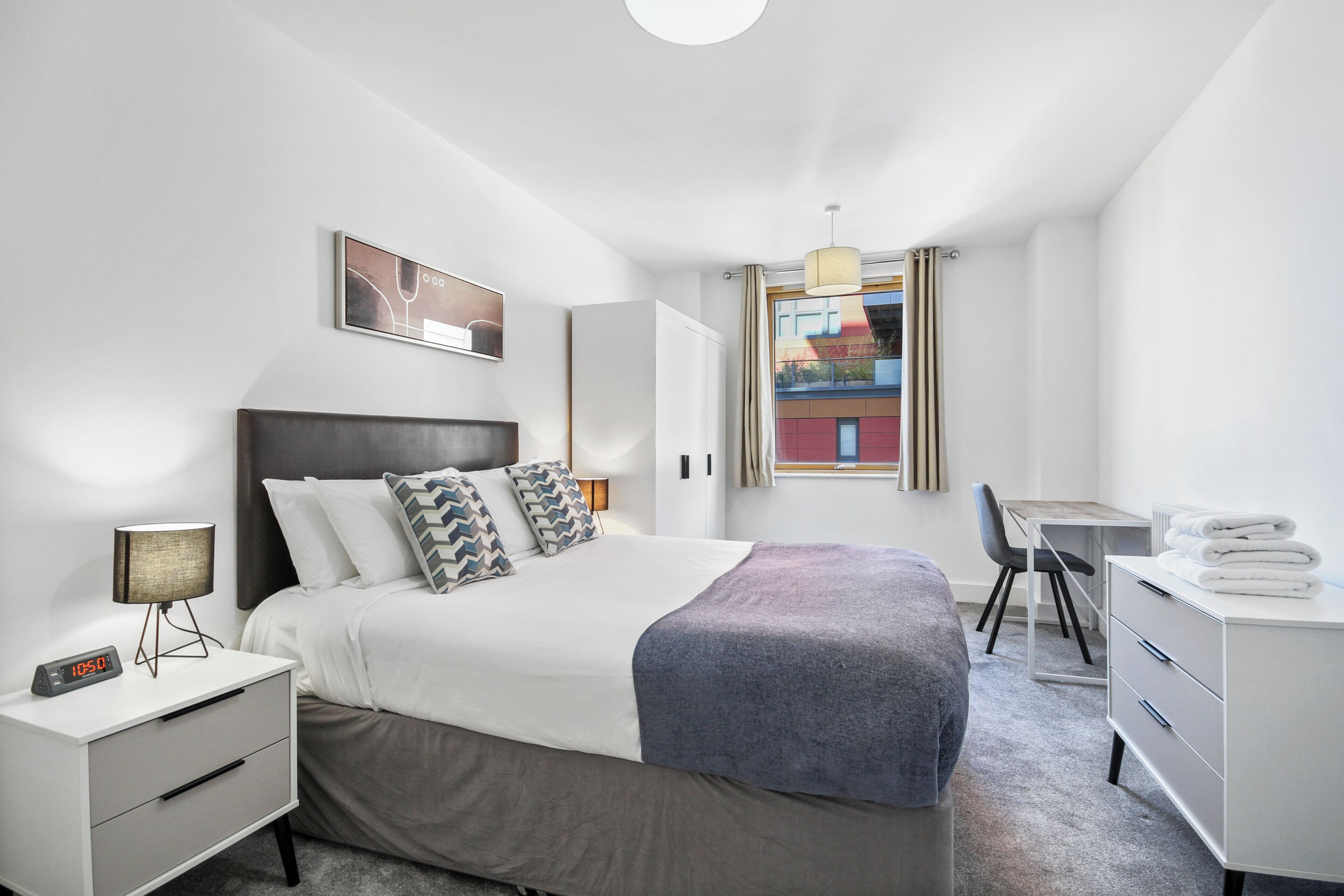Et moderne hotelværelse med seng, natbord, skrivebord og stol.