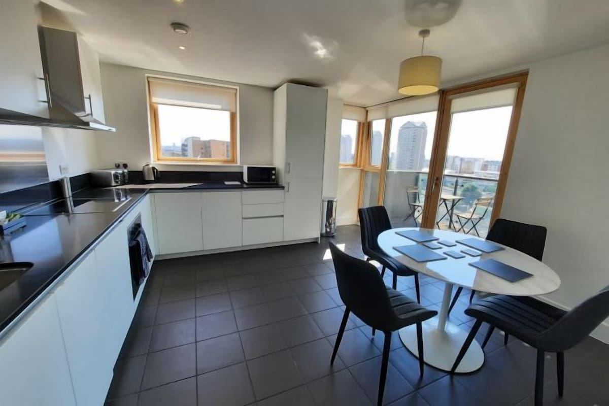 A modern kitchen with white cabinets, a black countertop, and a dining area with a round table and black chairs.
