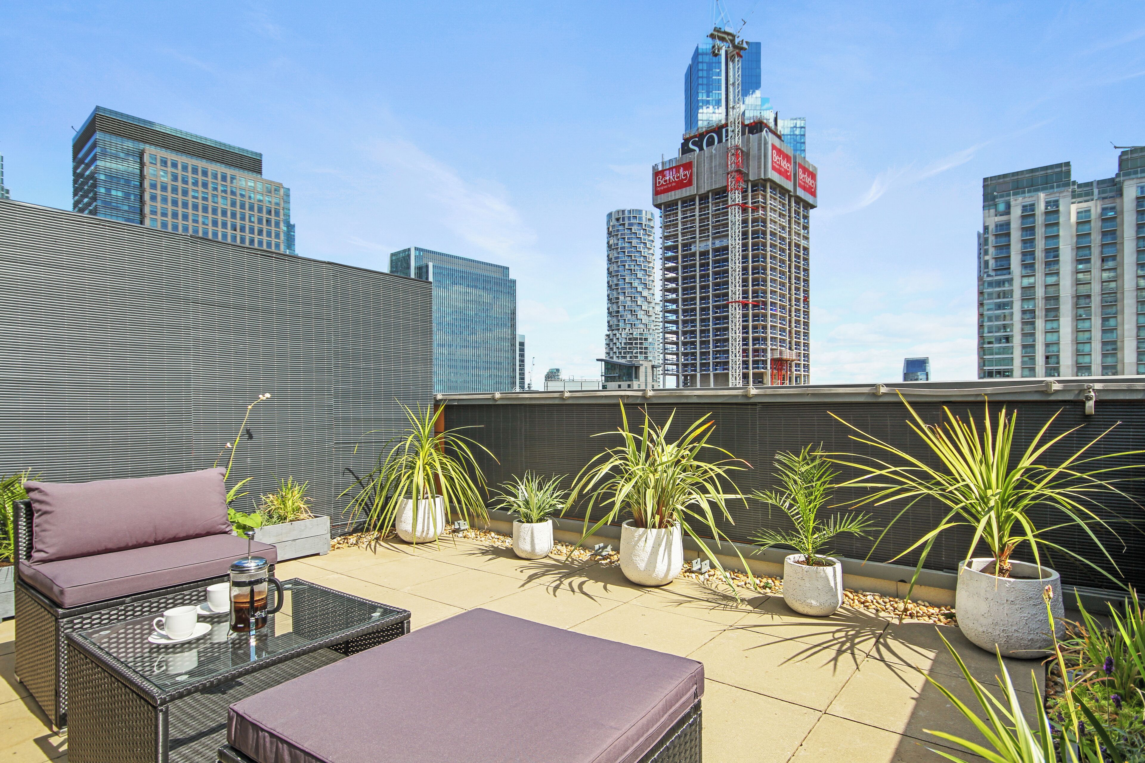 Una terraza en la azotea con mobiliario exterior, plantas en macetas y vistas panorámicas de la ciudad.