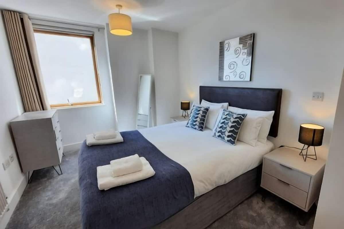 A modern hotel room with a large bed, bedside tables, a desk, and a window.