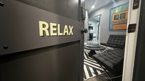A room with a 'RELAX' sign, a black leather sofa, and a patterned floor. - Stay At Jimmy's (Woodstock)