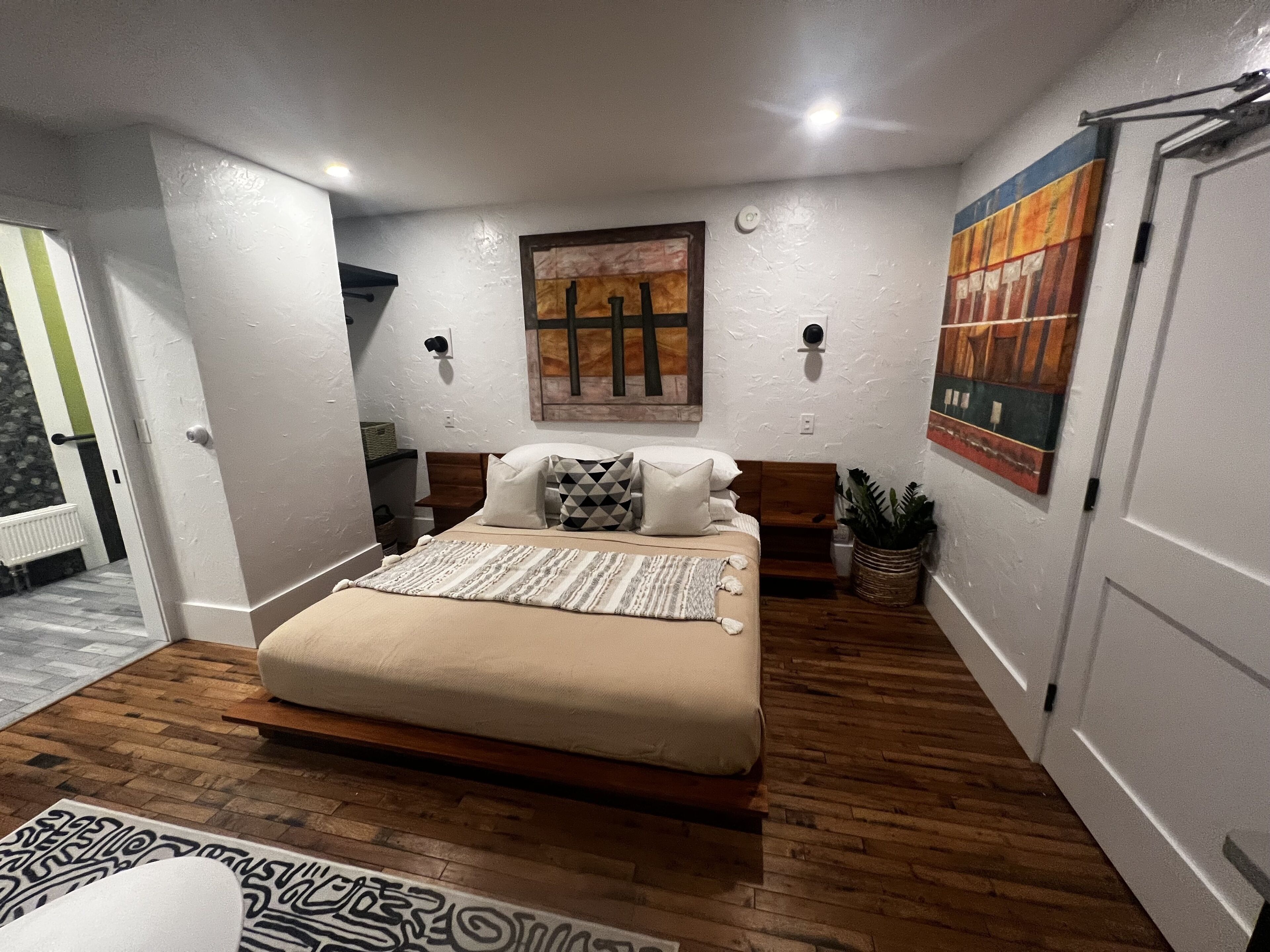 Une chambre à coucher avec un lit, un plancher en bois, des murs blancs et des œuvres d’art.