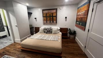 Une chambre à coucher avec un lit, un plancher en bois, des murs blancs et des œuvres d’art.