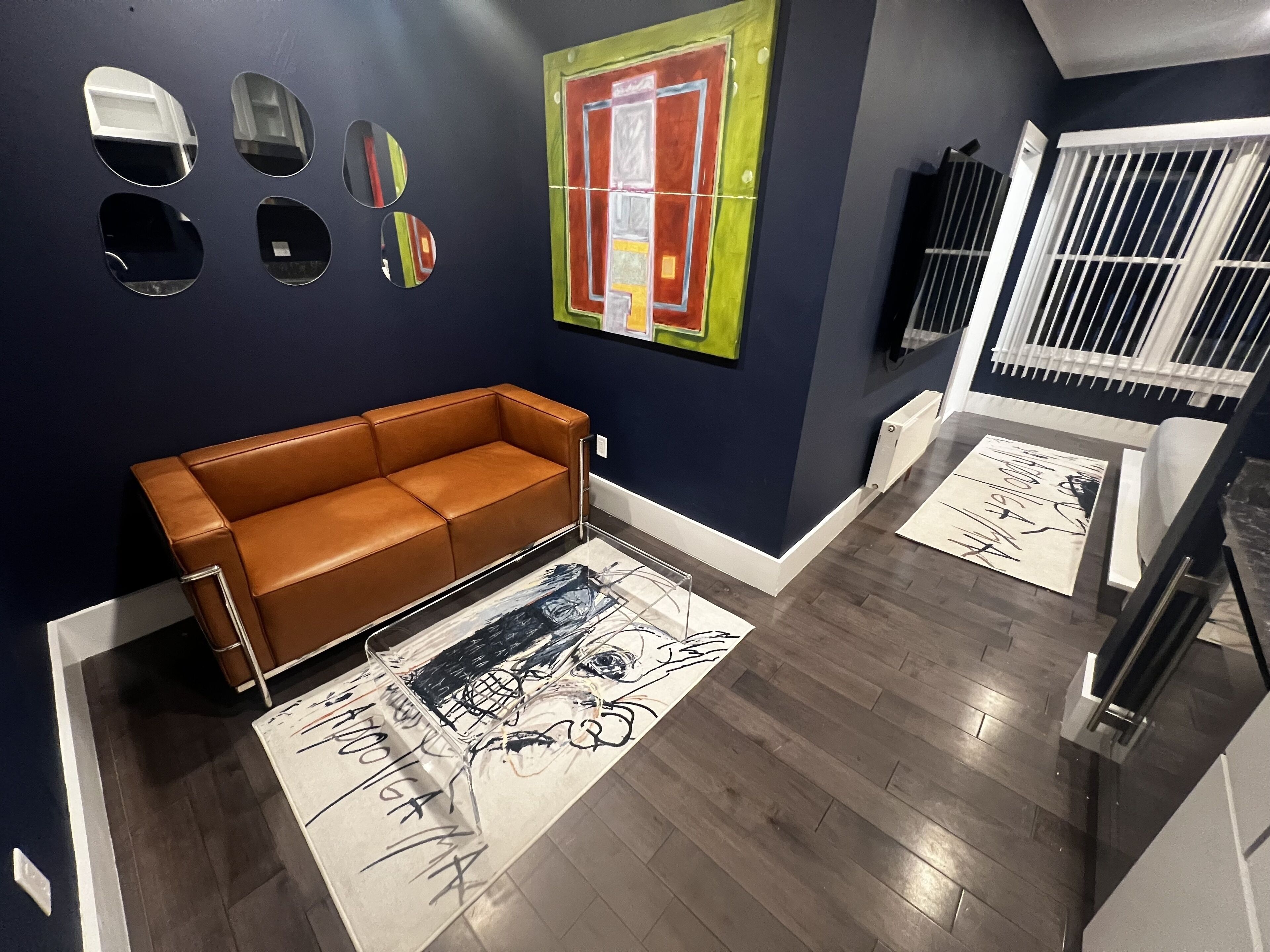 A modern living room with a brown leather sofa, a large abstract painting, and a patterned rug.