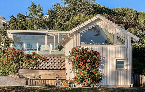 Ein modernes Haus mit einem großen Glasfenster, einer Holzterrasse und einem Garten mit roten Blumen.