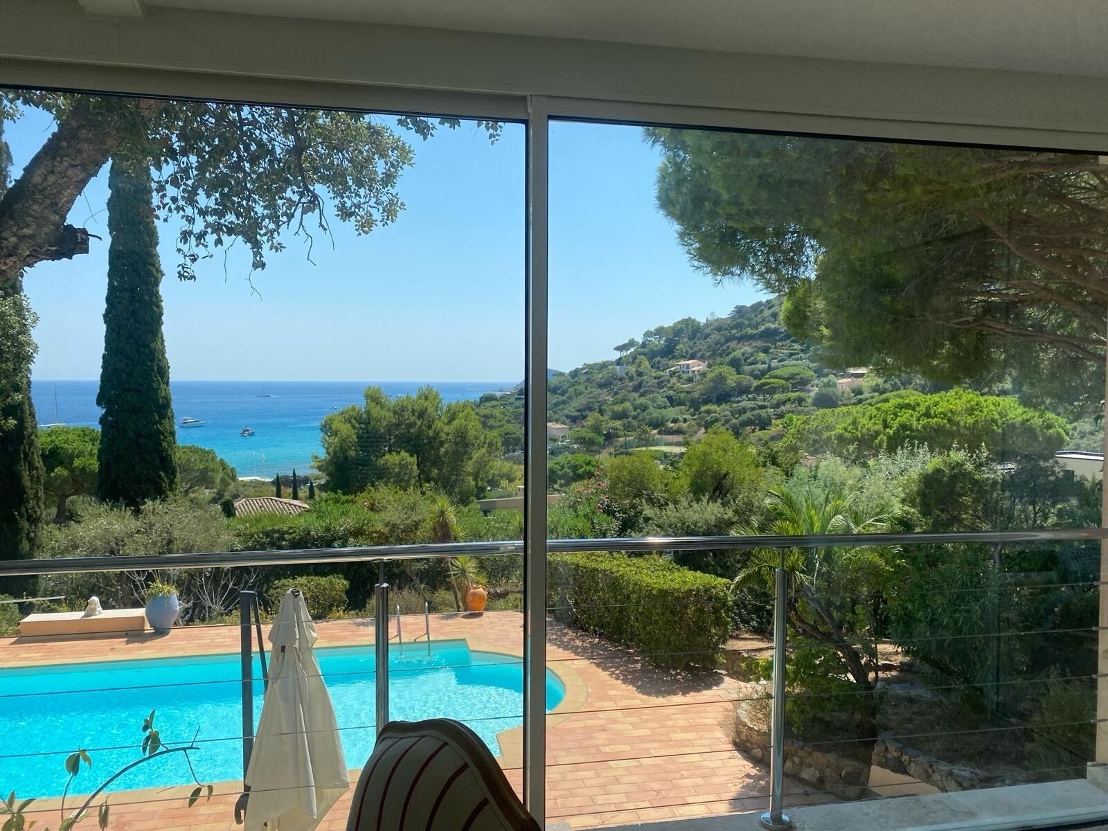 A balcony with a clear view of a swimming pool, lush greenery, and a distant coastline.