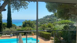 Un balcón con vista despejada a una piscina, abundante vegetación y una costa lejana.