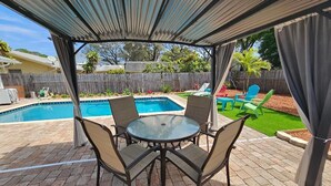 Ein überdachter Patio-Bereich mit Pool, Sitzgelegenheiten im Freien und Blick auf den Garten.