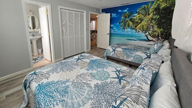 Ein Schlafzimmer mit zwei Betten, einem Deckenventilator, einem Wandbild mit Strandmotiv und einem begehbaren Kleiderschrank.