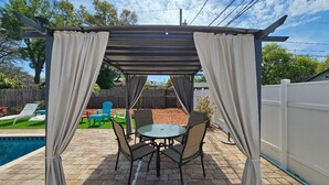 Eine Terrasse im Freien mit einer Pergola, einem Pool und einem Tisch mit Stühlen.