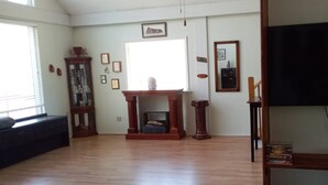 A spacious living room with hardwood flooring, a fireplace, a television, and a bookshelf. - Forest Get Away! Surrounded by National Forest. Beautiful home in the woods.  (Mena)