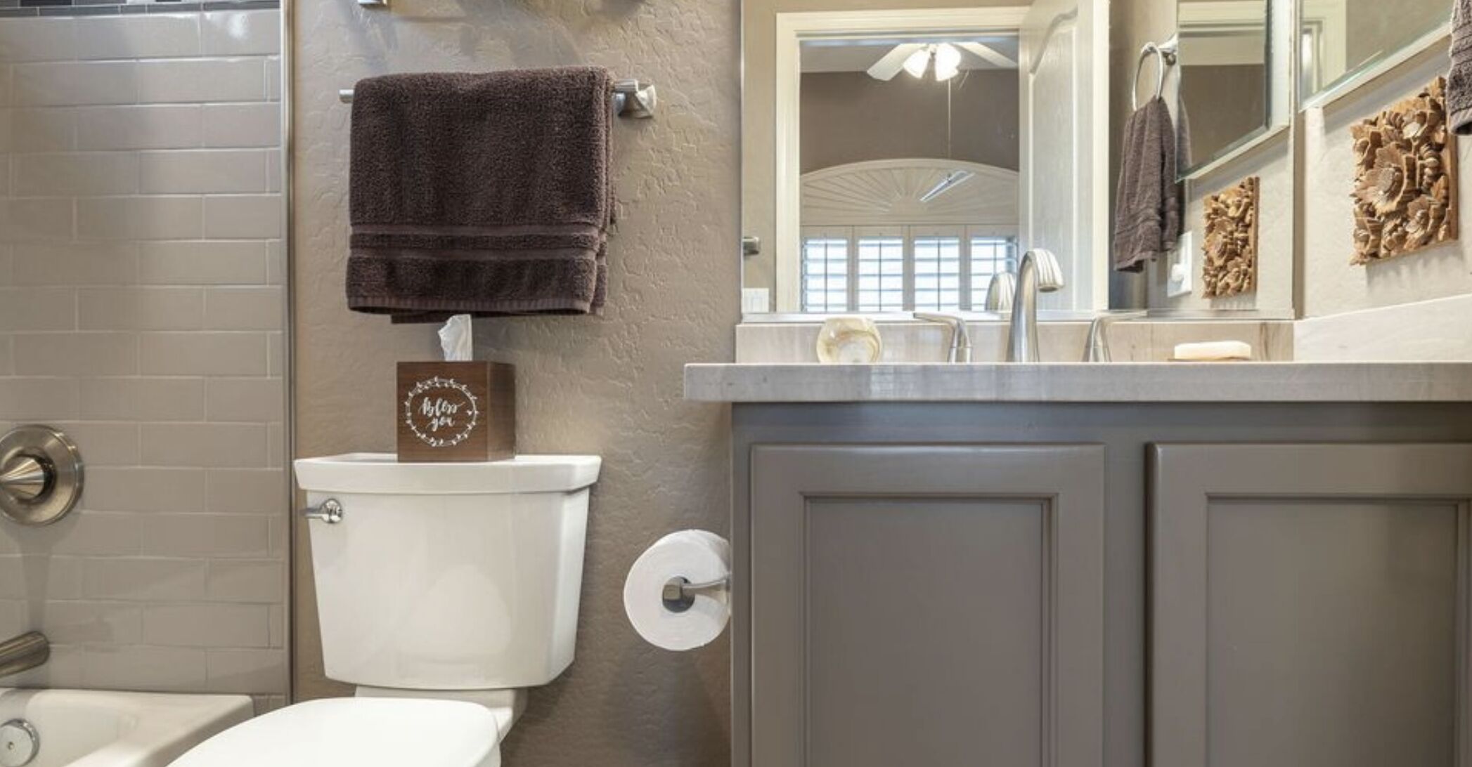 A bathroom with a toilet, a towel hanging on the wall, a tissue box, and a mirror above the sink.