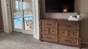 A room with a wooden dresser, a flat-screen TV, and a sliding glass door leading to a pool area. - 🌵 Anthem Country Club Retreat.  Heated Saltwater Pool, Spa, Casita & Office. (New River)