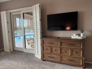 Een kamer met een houten dressoir, een flatscreen-tv en een glazen schuifdeur naar een zwembad.