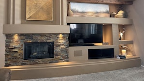 A modern living room with a stone fireplace, a flat-screen TV, and decorative items on shelves. - 🌵 Anthem Country Club Retreat.  Heated Saltwater Pool, Spa, Casita & Office. (New River)