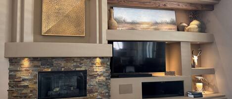 Ein modernes Wohnzimmer mit Kamin aus Stein, einem Flachbildfernseher und Dekoration auf Regalen.