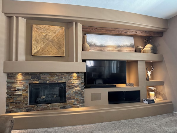 Een moderne woonkamer met een stenen openhaard, een flatscreen-tv en decoratieve objecten op planken.