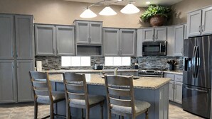 A modern kitchen with grey cabinets, a central island with bar stools, a stainless steel refrigerator, and a microwave. - 🌵 Anthem Country Club Retreat.  Heated Saltwater Pool, Spa, Casita & Office. (New River)