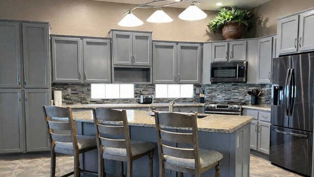 A modern kitchen with grey cabinets, a central island with bar stools, a stainless steel refrigerator, and a microwave. - 🌵 Anthem Country Club Retreat.  Heated Saltwater Pool, Spa, Casita & Office. (New River)