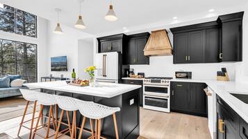 Une cuisine moderne avec des meubles noirs, un îlot central blanc et une grande fenêtre donnant sur une forêt.