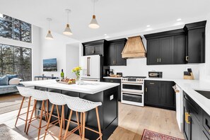 Une cuisine moderne avec des meubles noirs, un îlot central blanc et une grande fenêtre donnant sur une forêt.