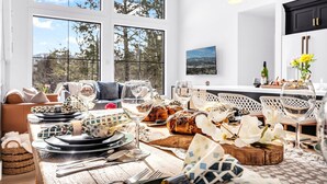 A dining area with a large window, a table set with plates, glasses, and a loaf of bread. - Unmatched Views of Sunday River! Slps 16! Hot Tub! (Newry)