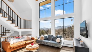 A spacious living room with a large window, a staircase, and a modern sofa. - Unmatched Views of Sunday River! Slps 16! Hot Tub! (Newry)