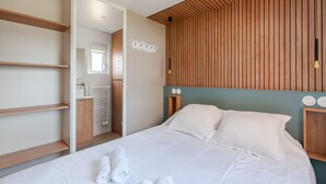 Une chambre d'hôtel moderne avec un lit bien fait, une tête de lit en bois, des étagères intégrées et une vue sur la salle de bain.