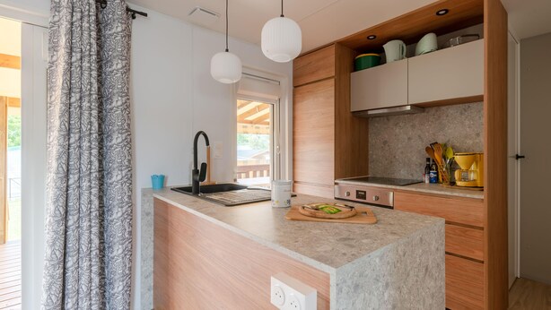 Une cuisine moderne dotée d’un plan de travail en marbre, de meubles en bois et de luminaires suspendus.