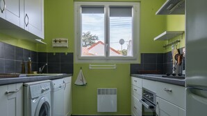 Une cuisine moderne avec des armoires blanches, un lave-linge intégré, un four double et une fenêtre donnant sur une maison.